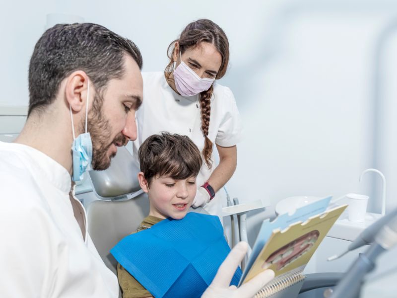 Odontología general: odontólogo general y asistente muestran un libro sobre los dientes a un paciente.