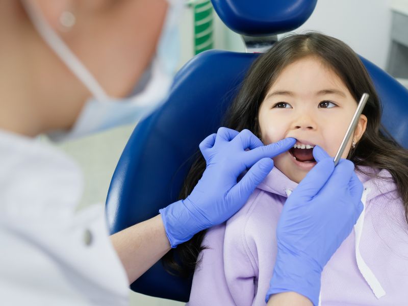 Niña en el sillón dental, odontopediatra revisa sus dientes